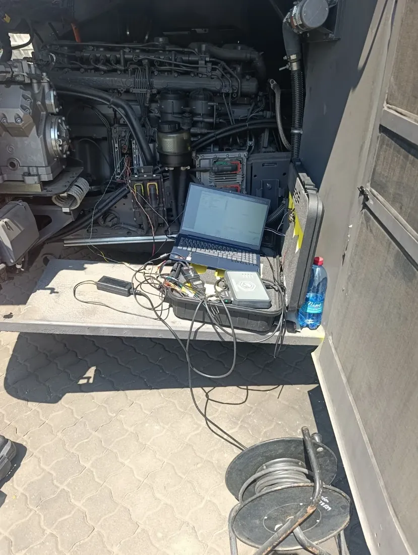 Laptop and ECU equipment connected beside an open Scania bus engine compartment
